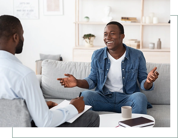 Cheerful black man talking to psychologist on meeting at his office, sharing his progress with doctor