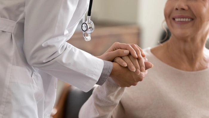 Close up shot of young female physician leaning forward to smiling elderly lady patient holding her hand in palms