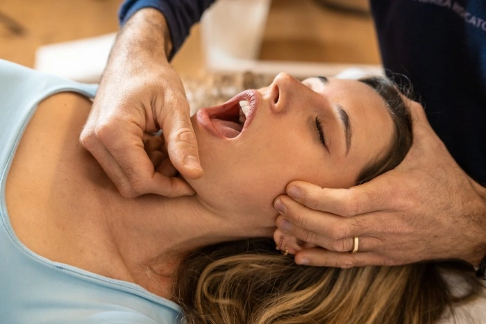 An osteopath performs a jaw adjustment on a female patient
