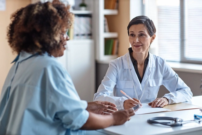 smiling woman gynecologist consulting African American female patient while sitting in clinic office
