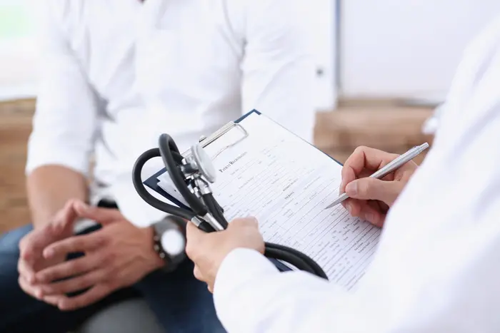 Male doctor hand hold silver pen filling patient history list at clipboard pad