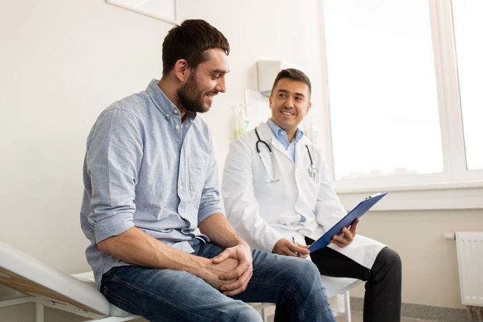 smiling doctor with clipboard and young man patient meeting at hospital