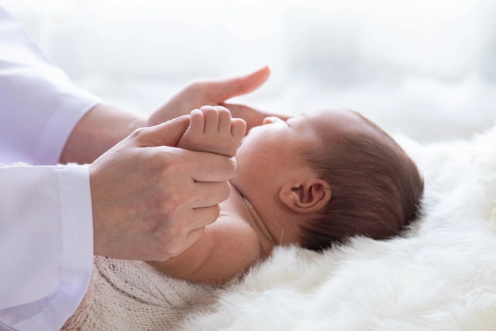 Doctor hand hold tiny newborn baby sick sleeping during examine by pediatrician doctor with stethoscope, doctor monitoring heart pulse rate adorable infant in clinic, baby health care concept